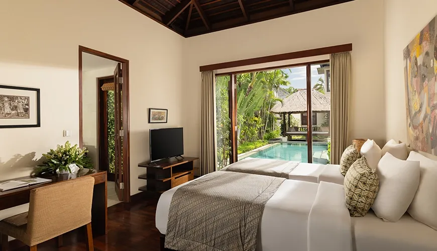 Elegant twin bedroom with wooden floors and a stunning view of a lush garden and pool at The Suar Seminyak