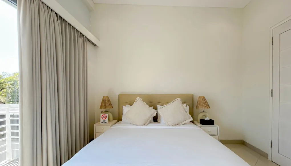 Modern bedroom with a king-size bed, a dresser, and a large window at The Suar Sanur