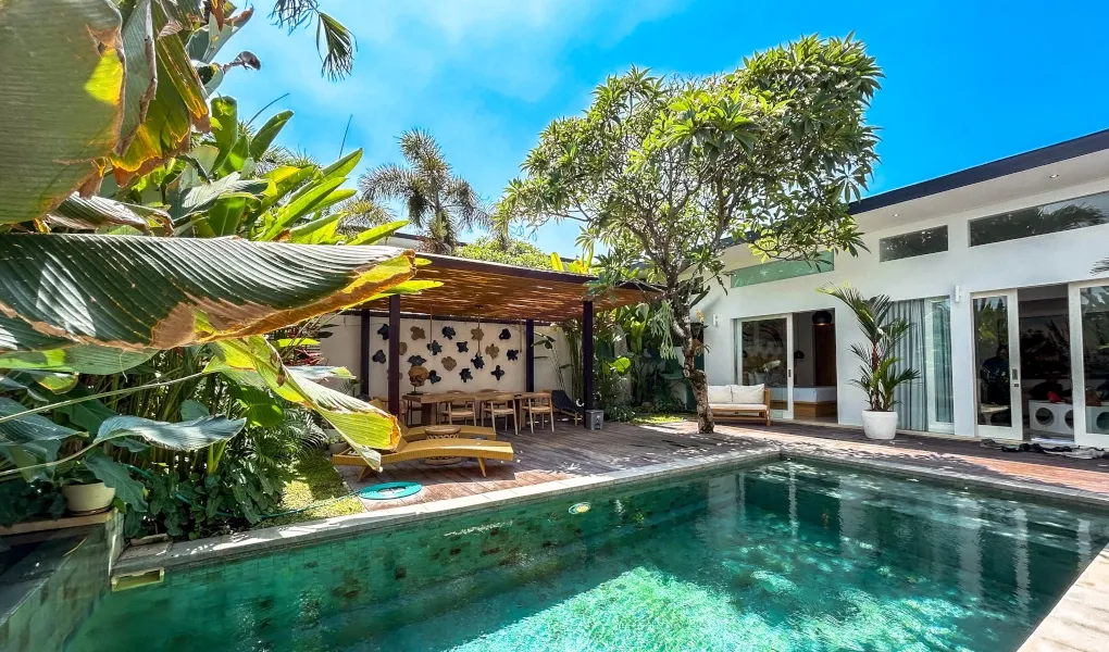 Tranquil swimming pool surrounded by lush greenery and lounge chairs at The Suar Sanur