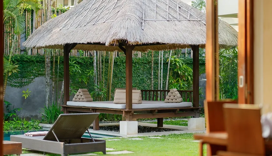 Traditional thatched roof gazebo with daybeds surrounded by lush garden at The Suar Seminyak