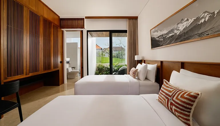 Spacious twin bedroom with two comfortable beds and a window showing a private outdoor area and rice fields at Uma Santai Canggu