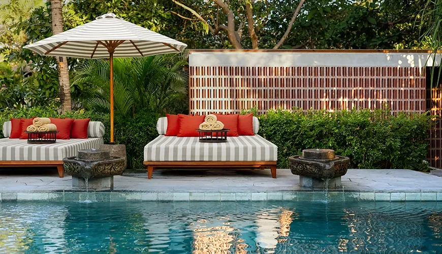 Luxurious poolside setting featuring crisp towels, vibrant orange pillows, and a large striped umbrella at Uma Santai Pererenan