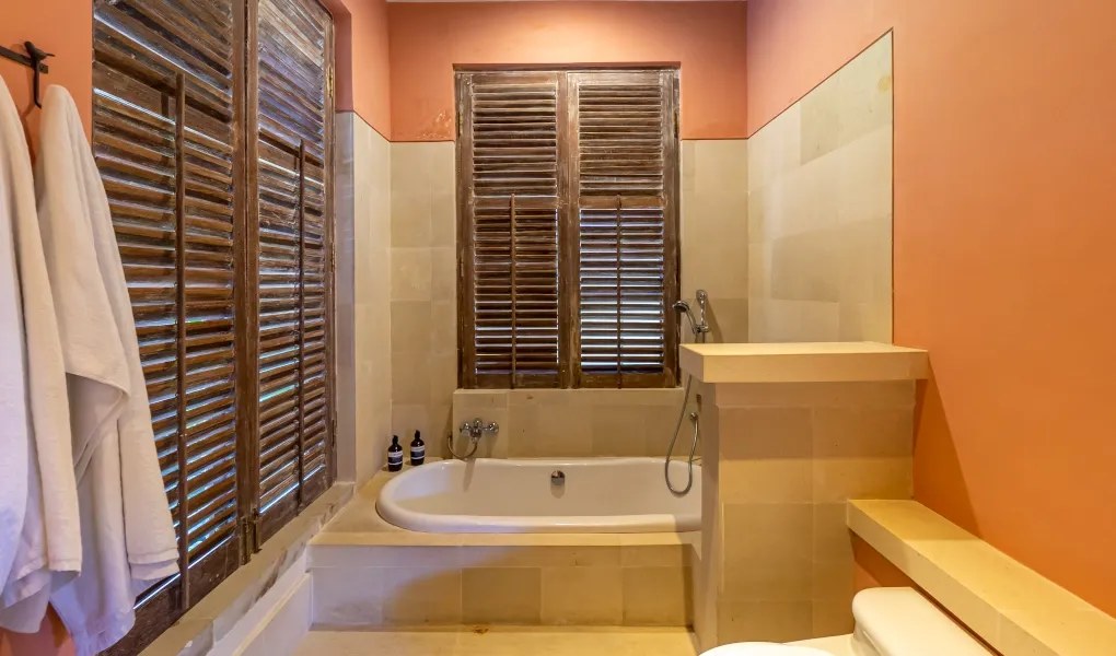 Rustic bathroom with a built-in tub and peach-colored walls at Villa Angsa