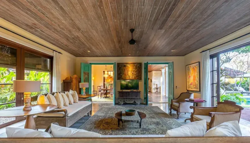 Spacious living area with tropical wooden ceilings, comfortable sofas, and a view to the pool at Villa Angsa.