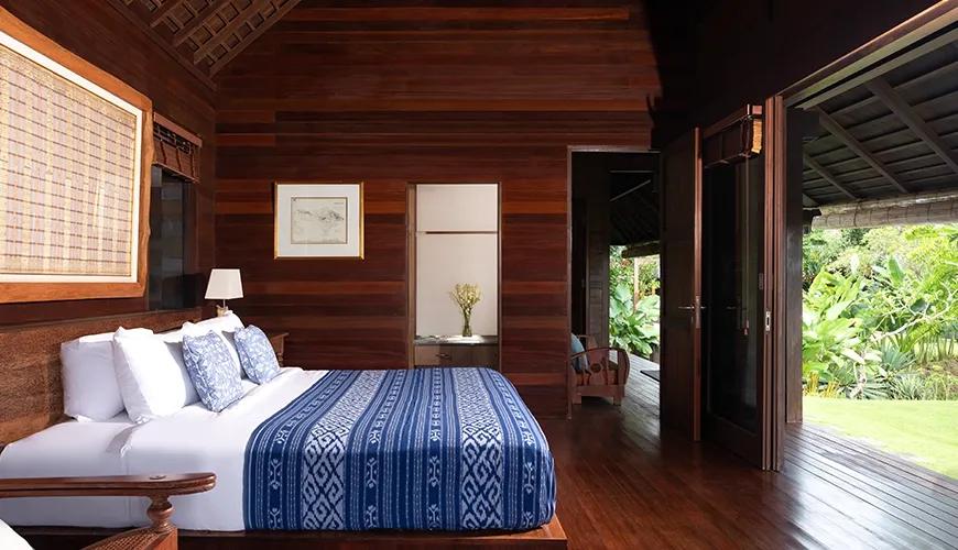 Luxurious wooden villa bedroom featuring a large bed with blue patterned linens and garden view access at Villa Bangkuang