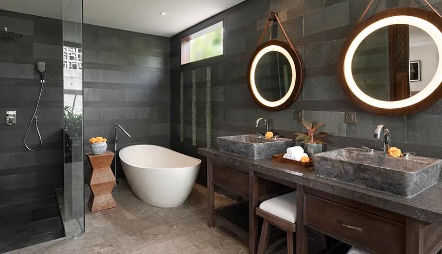 Modern luxury villa bathroom with dark stone walls featuring a white soaking tub and dual vanities at Villa Bangkuang