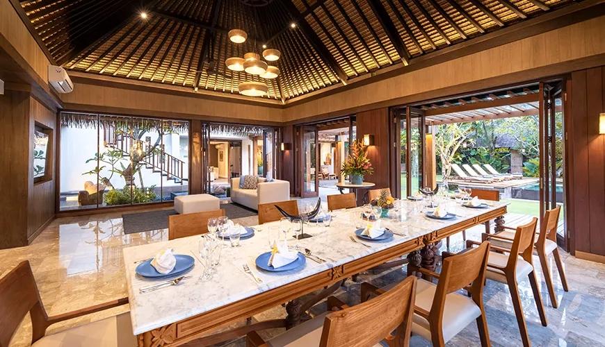 Open plan villa dining room with a large wooden table overlooking the outdoor swimming pool area at Villa Bangkuang