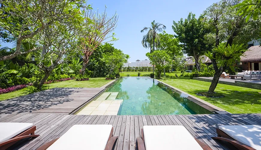 Stunning private infinity pool surrounded by a large wooden deck, comfortable loungers, and tropical gardens at Villa Bangkuang