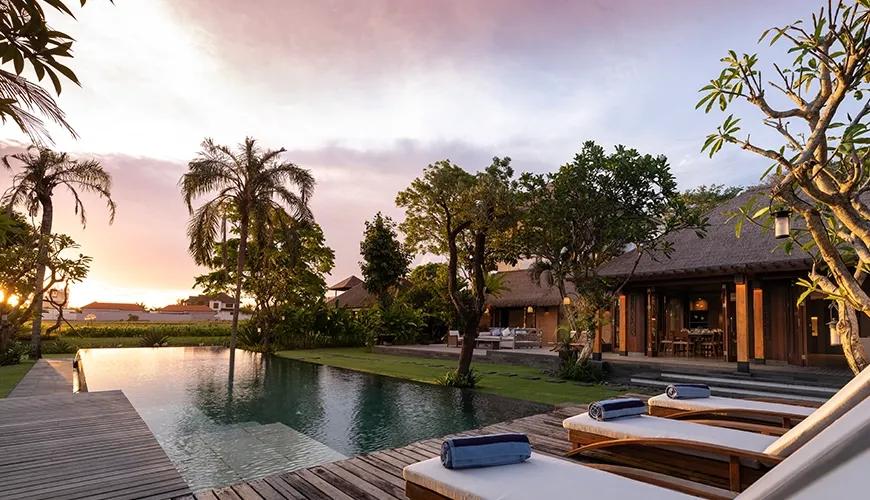 Sunset view of a luxury villa swimming pool with glowing lights and white sun loungers at Villa Bangkuang