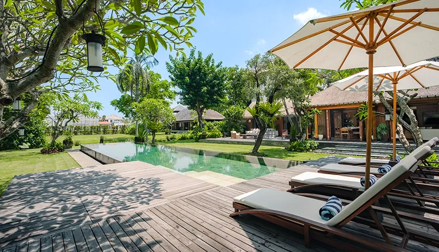 Tropical resort pool area featuring an infinity edge, green manicured lawn, and beautiful dense foliage at Villa Bangkuang