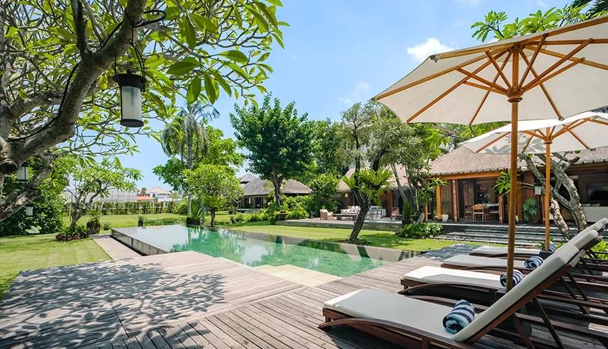Wide view of a sparkling villa swimming pool with comfortable sunbeds under umbrellas and tropical trees at Villa Bangkuang