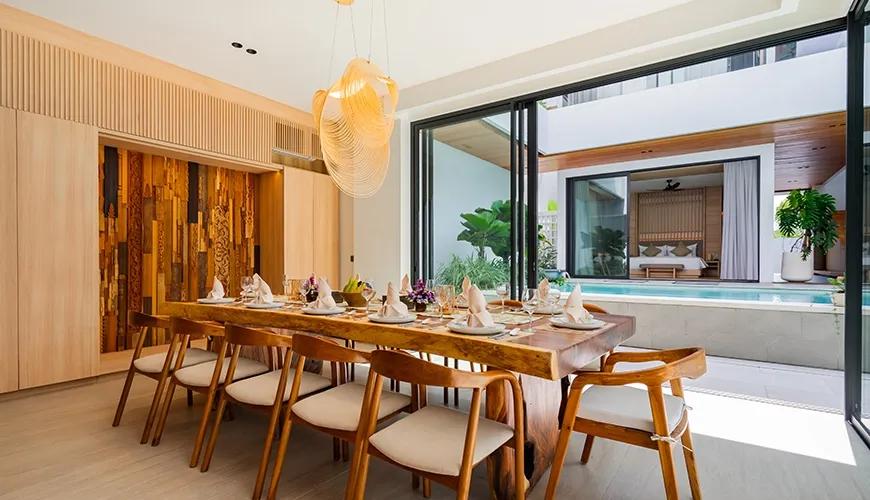 Elegant wooden dining table with place settings overlooking a private swimming pool through large glass doors at Villa Brandon