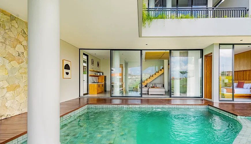Inviting teal swimming pool with a modern stone column and floor-to-ceiling glass doors opening inside at Villa Chanthira Luxe