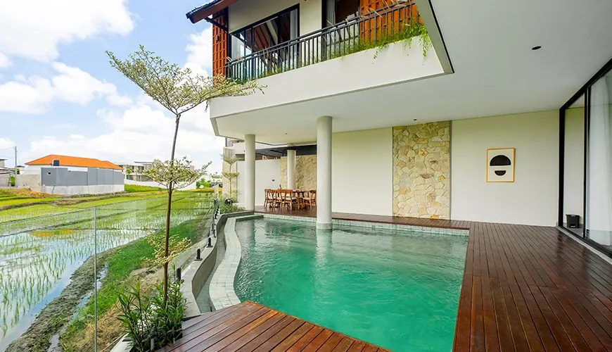 Luxury villa exterior featuring a teal swimming pool, stone accent wall, and spacious second-floor balcony at Villa Chanthira Luxe