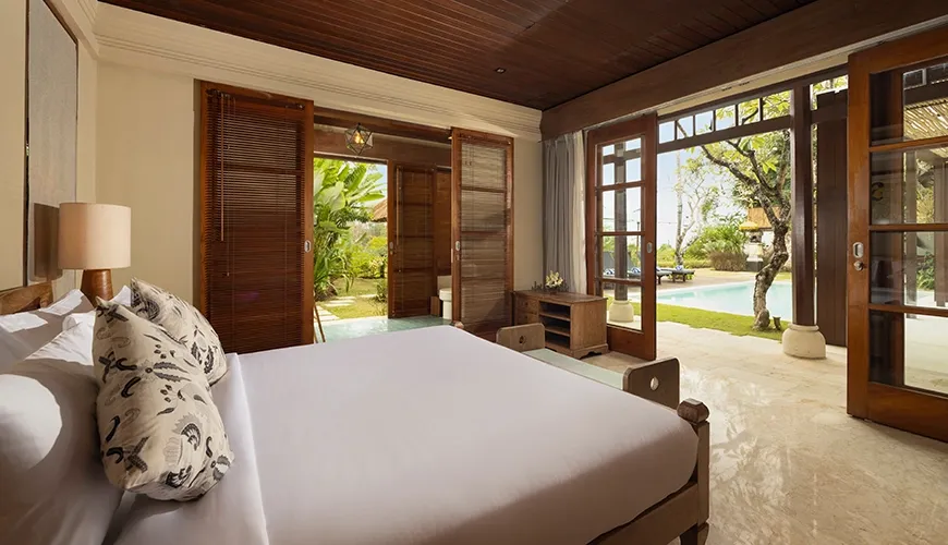 Elegant villa bedroom with a dark wooden ceiling, marble floors, and sliding glass doors opening directly onto the swimming pool at Villa Grasshopper