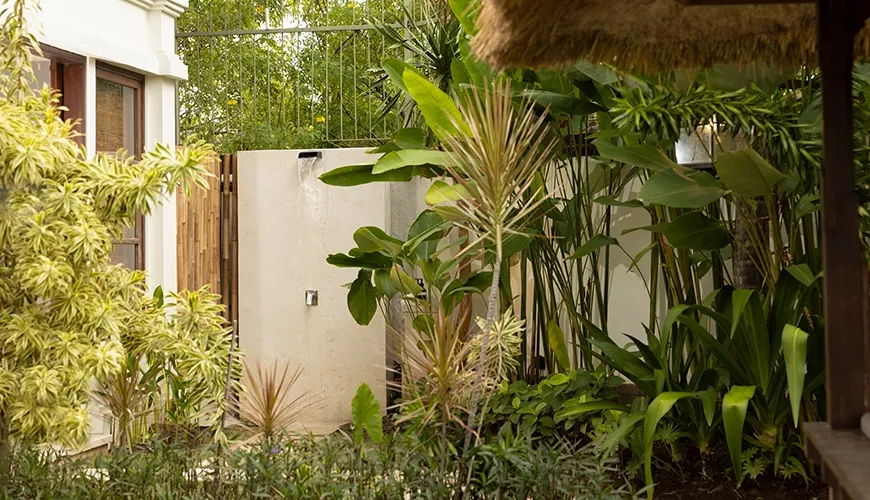 Lush green garden area featuring a modern stone outdoor shower surrounded by tropical plants and foliage at Villa Grasshopper