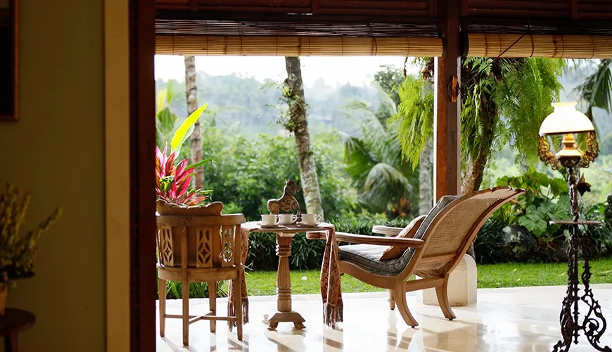 Tranquil wooden villa terrace bathed in soft morning light, with traditional rattan furniture and lush green surroundings at Villa Inka