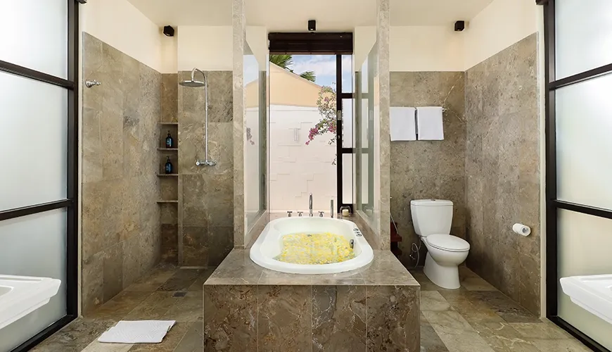 Luxurious modern bathroom featuring a stone bathtub filled with yellow flowers and a walk-in shower at Villa Jamalu