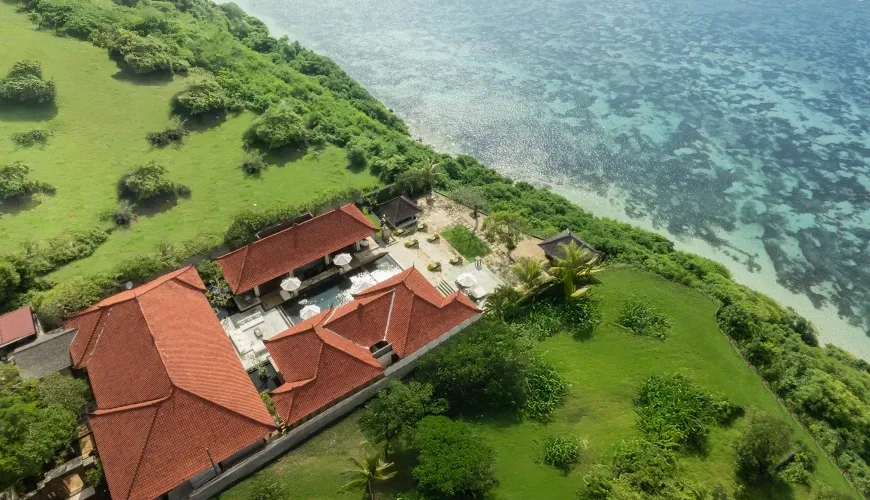 Aerial view of a villa with a red-tiled roof perched on a cliffside overlooking the ocean at Naga Sutra Villa
