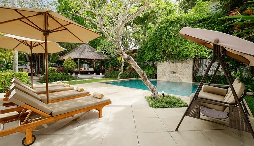 Beautiful outdoor pool area with sun loungers, umbrella shade, and a traditional thatched pavilion surrounded by tropical plants at Villa Ohm