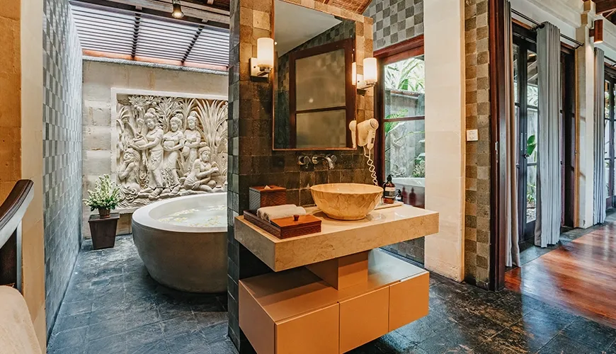 Ornate villa bathroom featuring a deep stone bathtub, artistic wall carvings, and a modern floating vanity at Villa Pulung Jimbaran