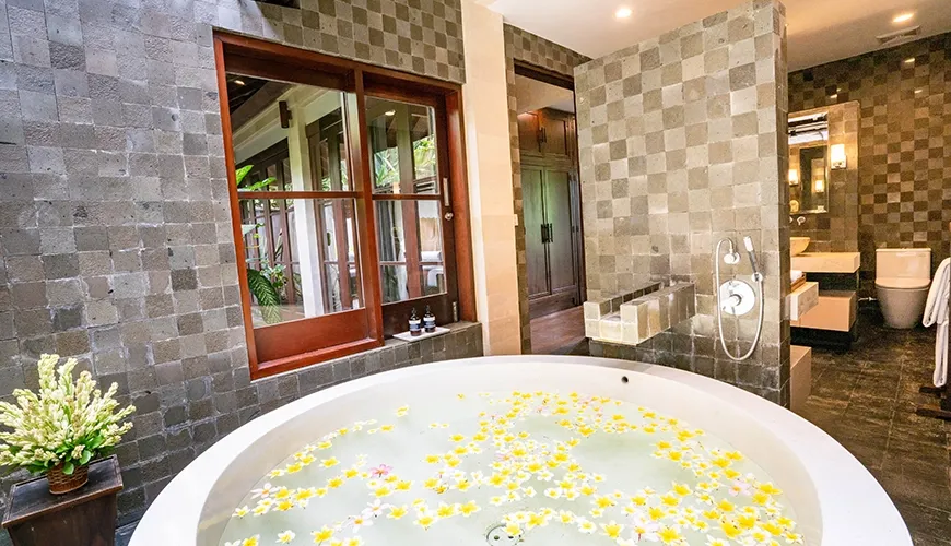 Tranquil villa bathroom with a large round bathtub filled with floating yellow and white flowers at Villa Pulung Jimbaran