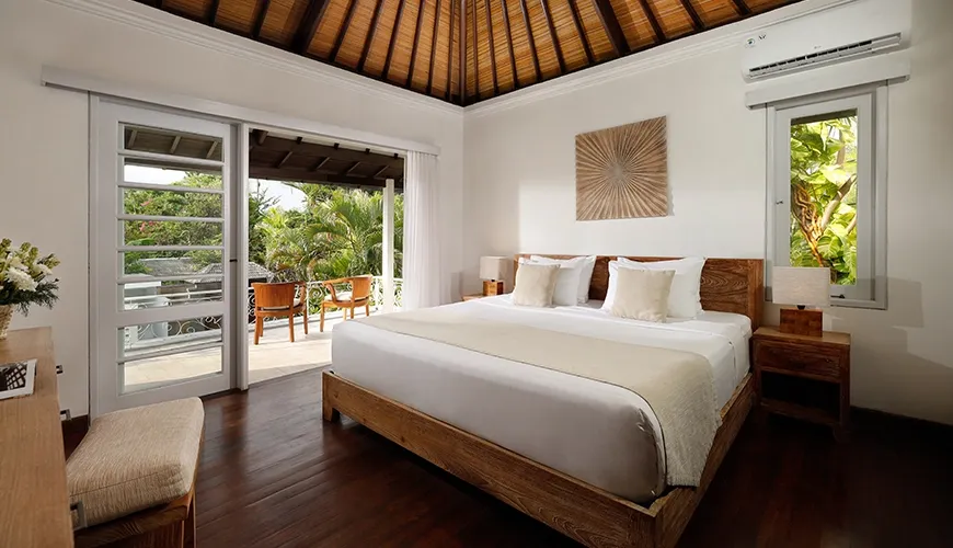 Cozy villa bedroom featuring a king-sized bed and a private balcony with two comfortable chairs overlooking the patio at Villa Swarna