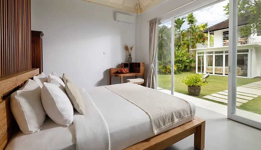 Minimalist bedroom with a large window and sliding glass door that opens to a private villa garden at Villa Swarna