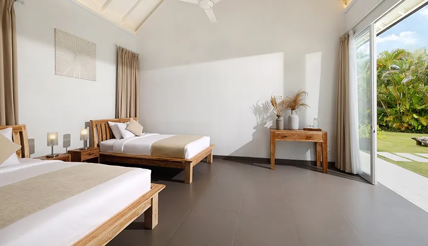 Spacious twin bedroom featuring two beds with wooden frames and a beautiful view of a lush outdoor space at Villa Swarna
