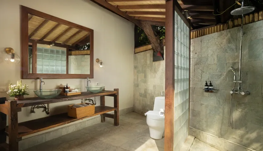 Balinese-style bathroom with stone walls and wooden vanity at Villa Tirtadari