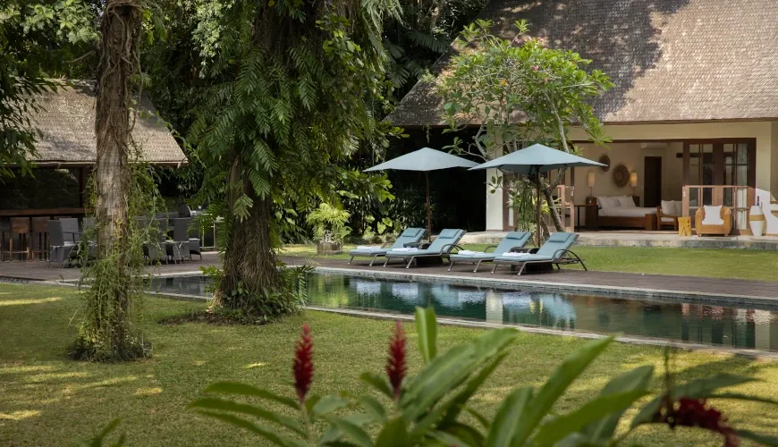 Lush garden with a long narrow pool and sun loungers at Villa Tirtadari