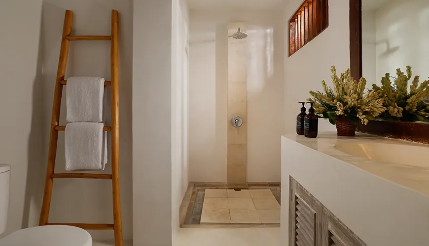 Bright villa bathroom featuring a modern walk-in rainfall shower light marble countertop and rustic wooden ladder accents at Villa Tropical Svasti.