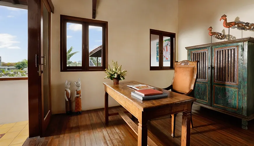 Dedicated villa office space featuring a vintage wooden desk comfortable chair and brightly colored antique cabinet at Villa Tropical Svasti