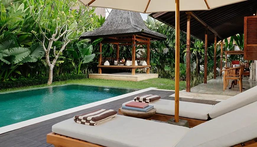 Relaxing poolside setting at a tropical villa including wooden deck chairs and a serene outdoor lounge pavilion at Villa Tropical Svasti