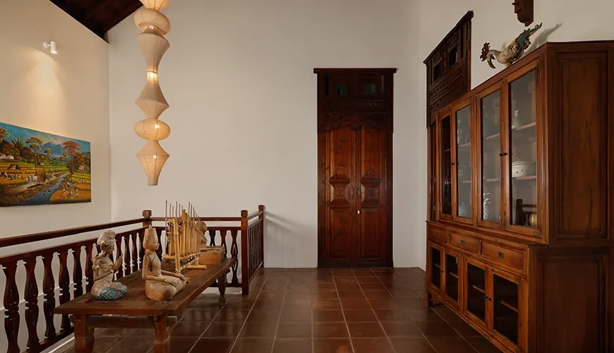 Second floor villa hallway showcasing beautiful traditional wood carvings elegant display cabinetry and tiered pendant lighting at Villa Tropical Svasti