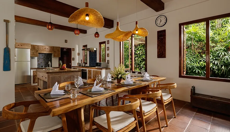 Spacious villa kitchen and dining room featuring a long natural wood table and rustic straw light fixtures at Villa Tropical Svasti