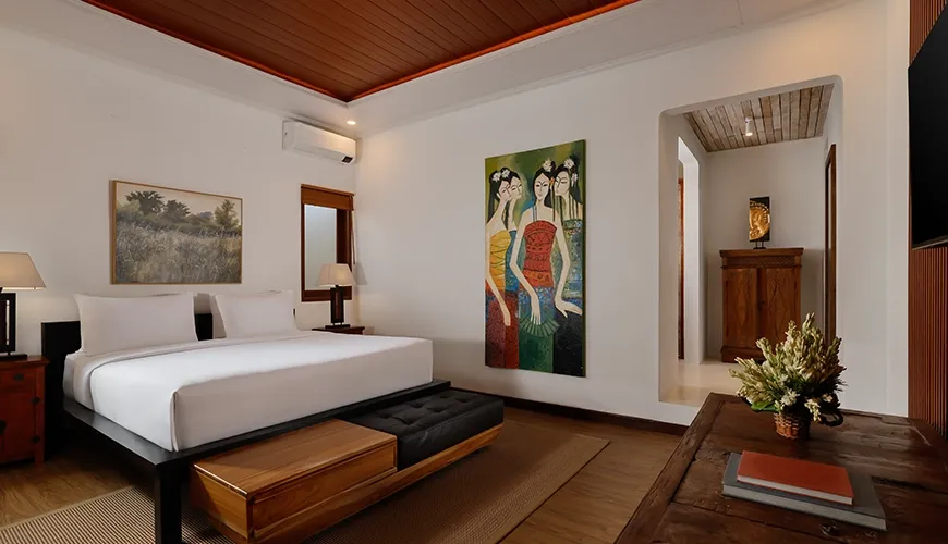 Stylish villa bedroom featuring a comfortable bed distinctive local artwork and beautiful warm wooden accents throughout the space at Villa Tropical Svasti