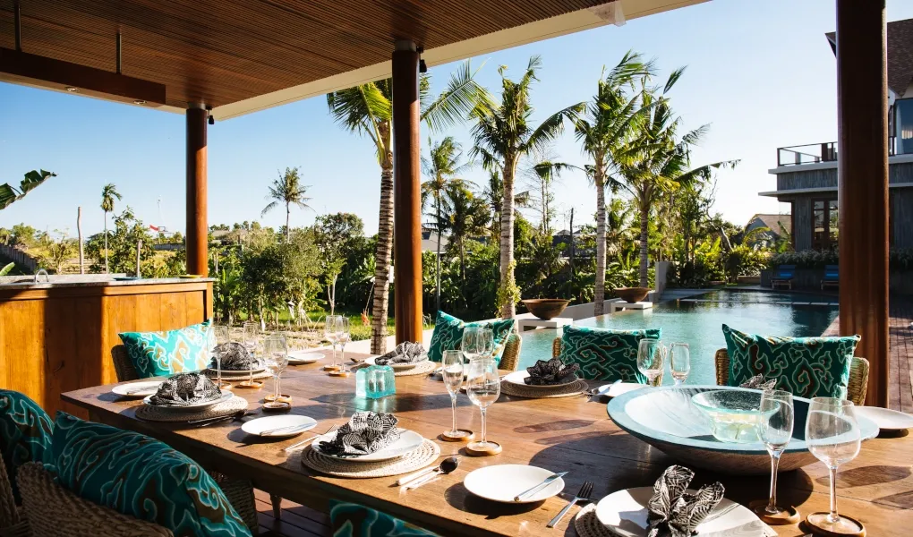 Outdoor dining area with a long table and turquoise pillows, by the pool at Villa Umah Daun
