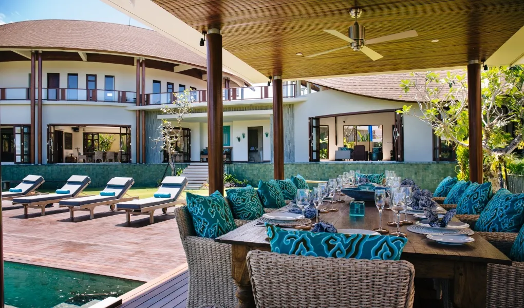 Outdoor dining table by the pool with turquoise chairs and garden view at Villa Umah Daun
