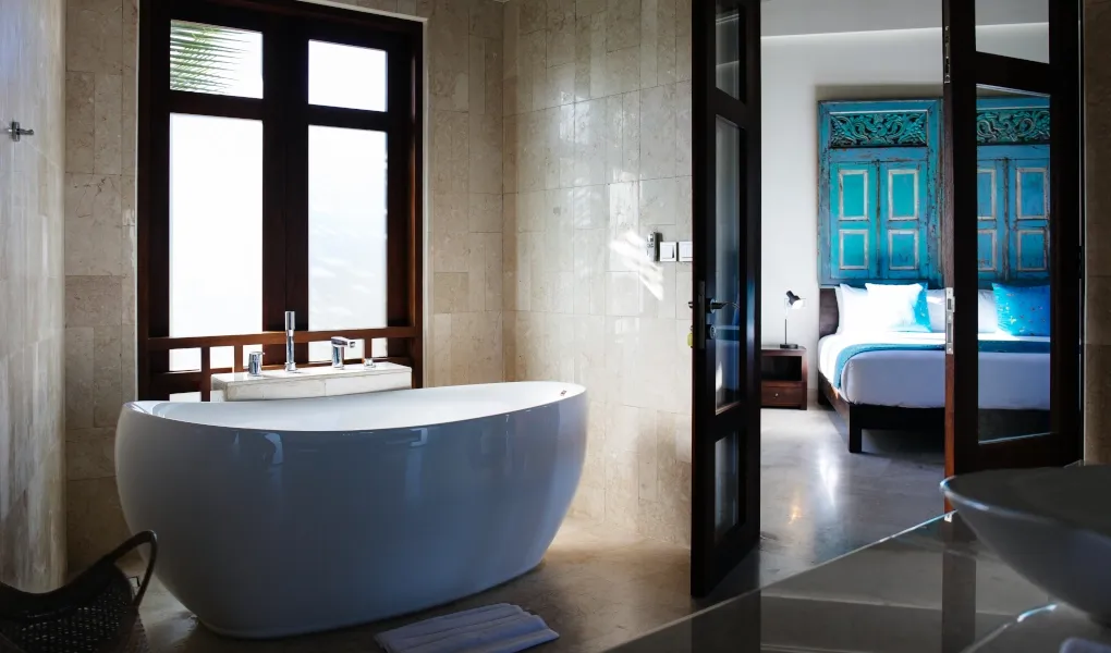 White bathtub with a view of the ensuite bedroom with turquoise doors at Villa Umah Daun