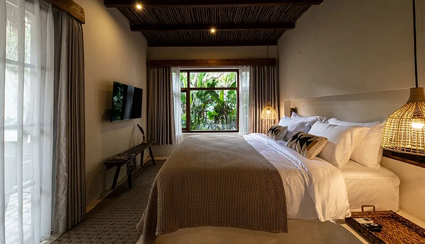 Cozy villa bedroom featuring a comfortable bed with crisp white linen, natural woven ceiling beams, and lush tropical jungle views through the window at Villa Xanadu