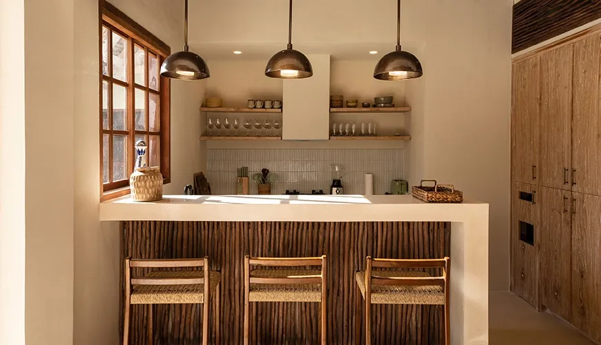 Modern villa bar area featuring three woven stools, a rustic wood counter, and minimalist shelving with contemporary copper pendant lights at Villa Xanadu