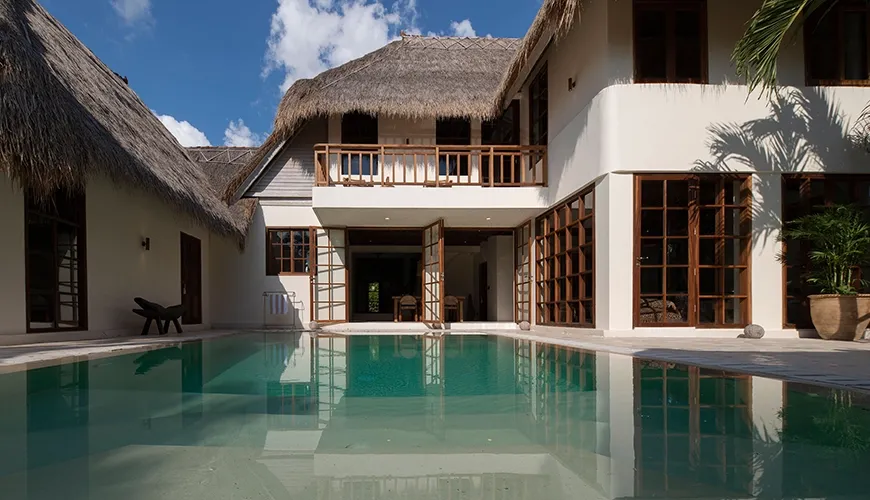 Stunning luxury villa exterior featuring traditional thatched roofs and a large private swimming pool under a bright blue sky at Villa Xanadu