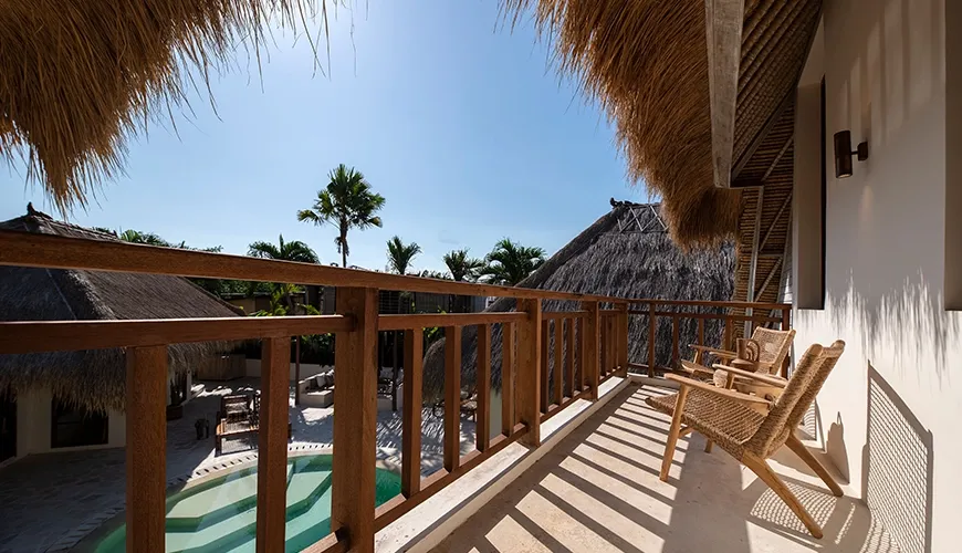 Sunny luxury villa balcony overlooking the curved private pool area, featuring thatched roofs and comfortable natural rattan chairs at Villa Xanadu