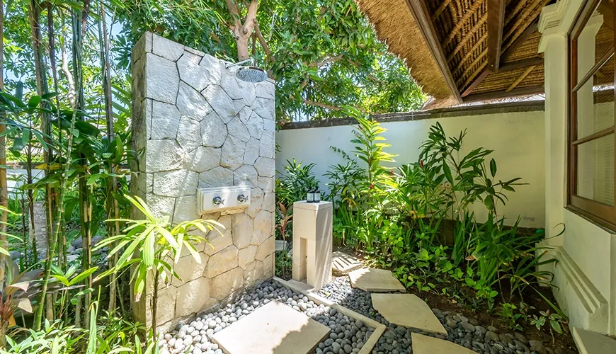 Beautiful and serene private outdoor shower with a rustic stone wall and lush green tropical plants at Villa Yasmine
