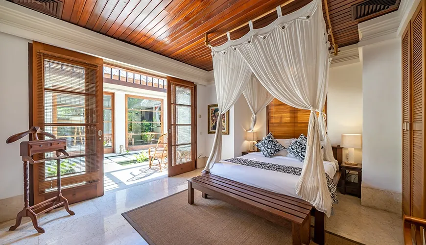 Luxurious villa bedroom with a wooden ceiling, a canopy bed, and large doors opening to a private outdoor garden at Villa Yasmine