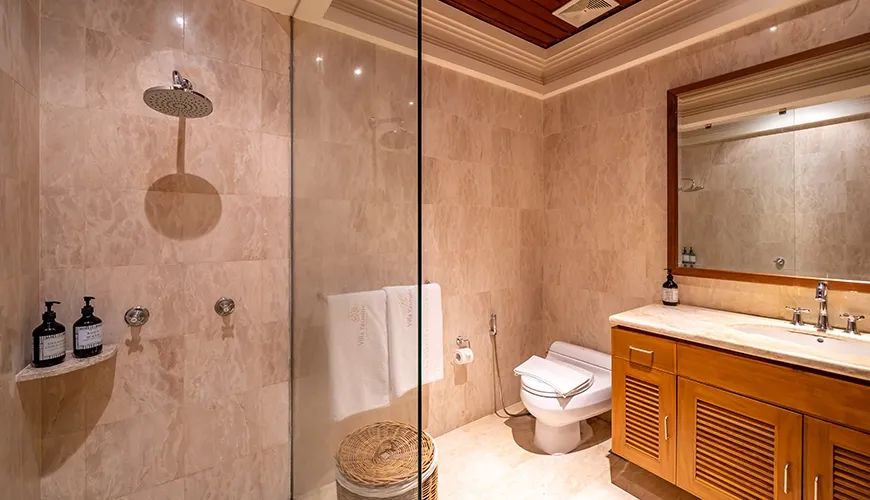 Spacious villa bathroom featuring a glass enclosed shower, a beautiful wooden vanity, and stunning marble tile at Villa Yasmine