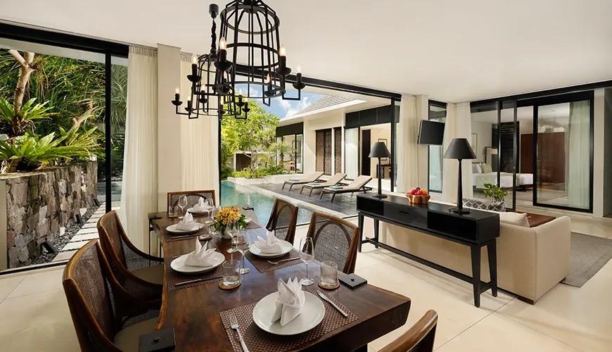 Open plan dining area featuring a wooden table and rattan chairs overlooking the tropical swimming pool at Vinila Villas Suite