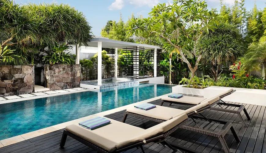 Private pool area with three sun loungers on a dark wood deck surrounded by greenery at Vinila Villas Suite